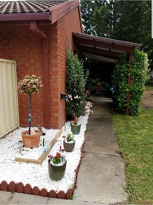 Tidy front garden bed with potted plants and white pebbles